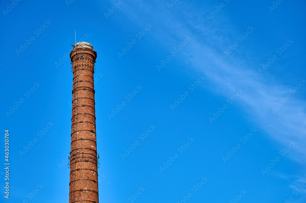 Smoke pipe made of bricks standing tall with white clouds and blue sky behind it during a summer day
