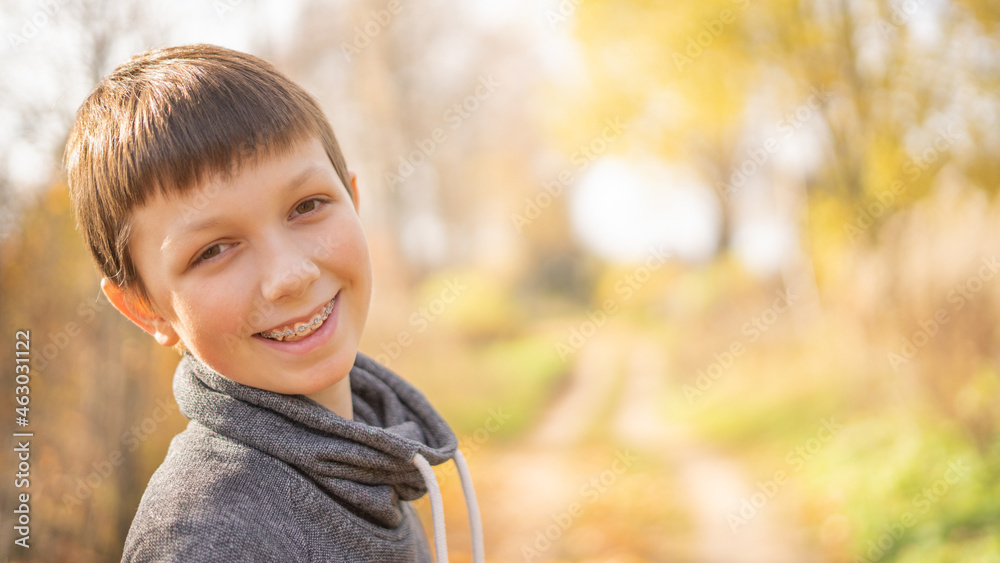 A cheerful teenager with braces on his teeth walks down the street on a bright day. Horizontally. A cheerful teenager with braces on his teeth walks down the street on a bright day. Horizontally.