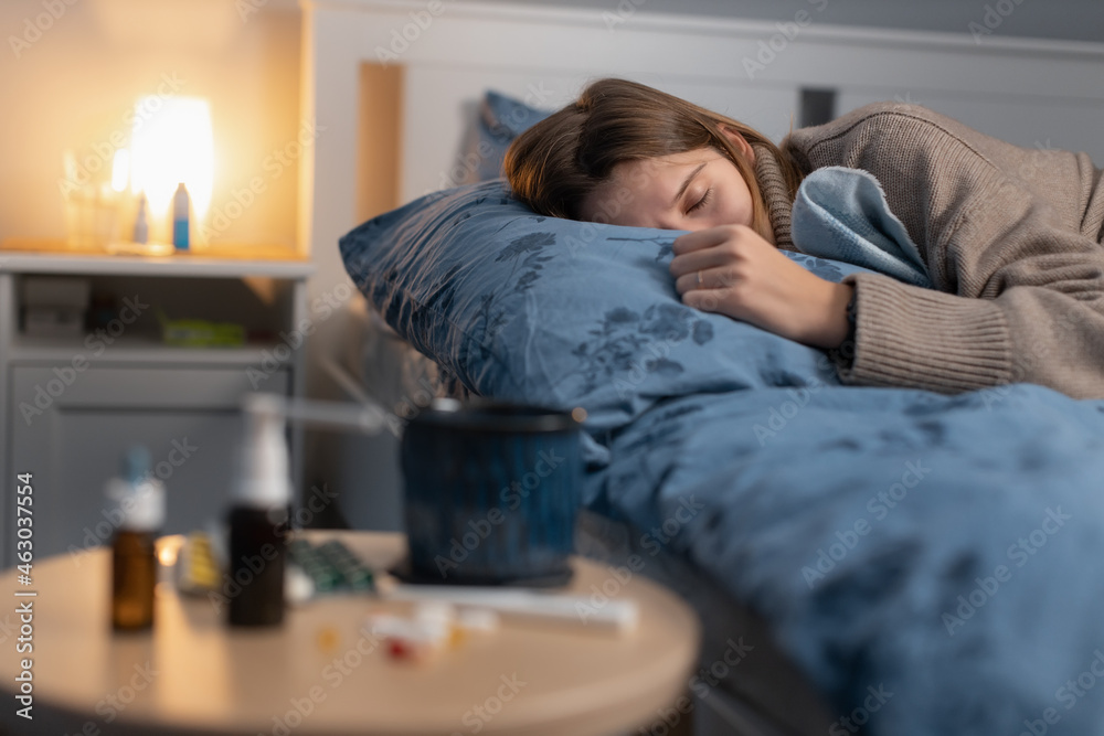 Obraz premium Illness girl sleeping in bed. Near table with various medicines and pills. Woman got the flu or a cold. Medications for nasal congestion and to reduce fever. Selective focus on female. Healthcare.