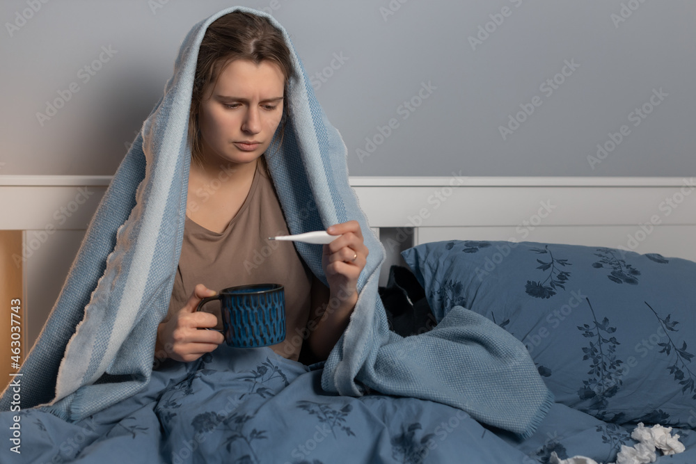 Caucasian girl covered with blanket sitting in bed, holding in hand