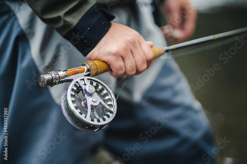 Closeup of fly-fisherman using rod with reel in river.