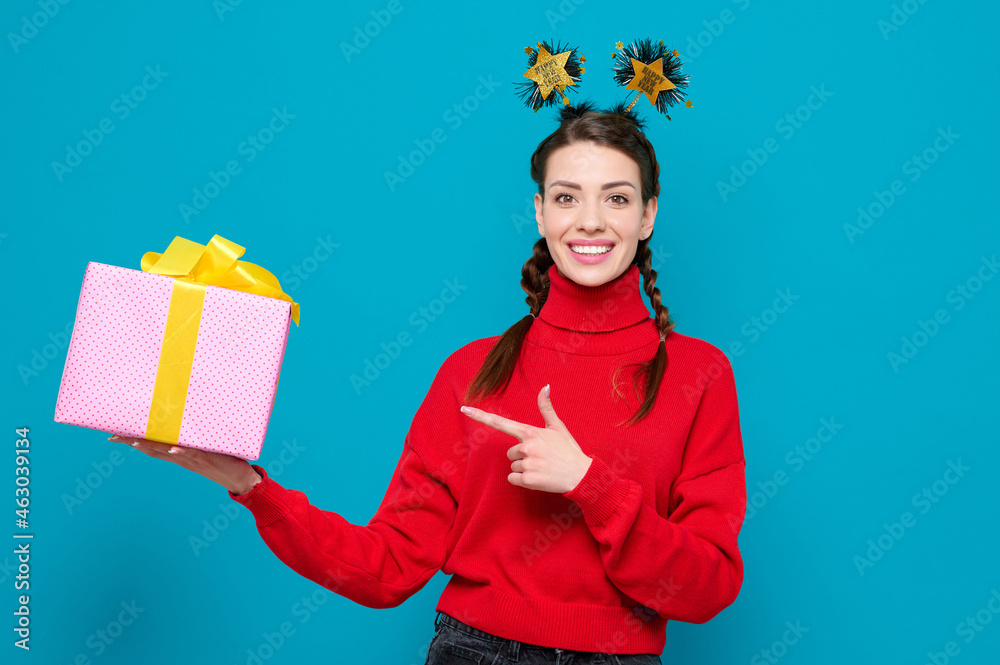 Happy smiling woman in red sweater celebrate new year party holds gift and point of finger to box on blue isolated background. Happy smiling woman in red sweater celebrate new year party holds gift and point of finger to box on blue isolated background.