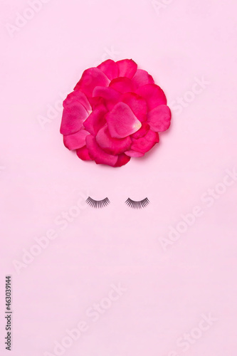 Creative woman face made of eyelashes and rose petals hair on the pink background. Minimal beauty concept. Makeup creative concept. Flat lay.