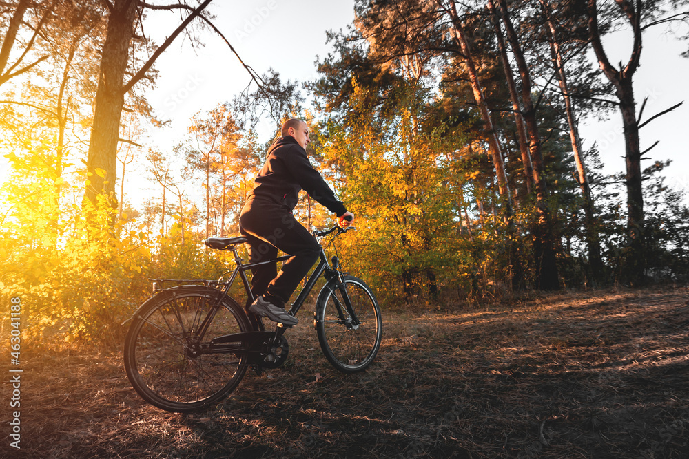 Man on a bike in the autumn forest in the evening at sunset