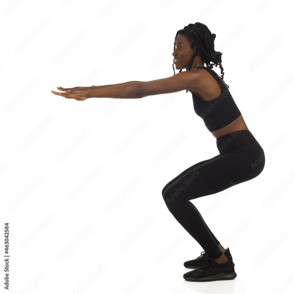 Woman in black sports clothes is doing a squat. Full length, side view. Woman in black sports clothes is doing a squat. Full length, side view.