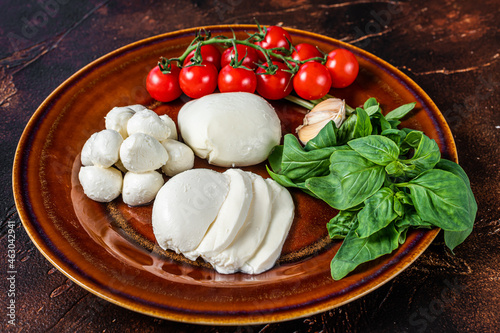 Mozzarella cheese, basil and tomato cherry ready for cooking Caprese salad. Dark background. Top view