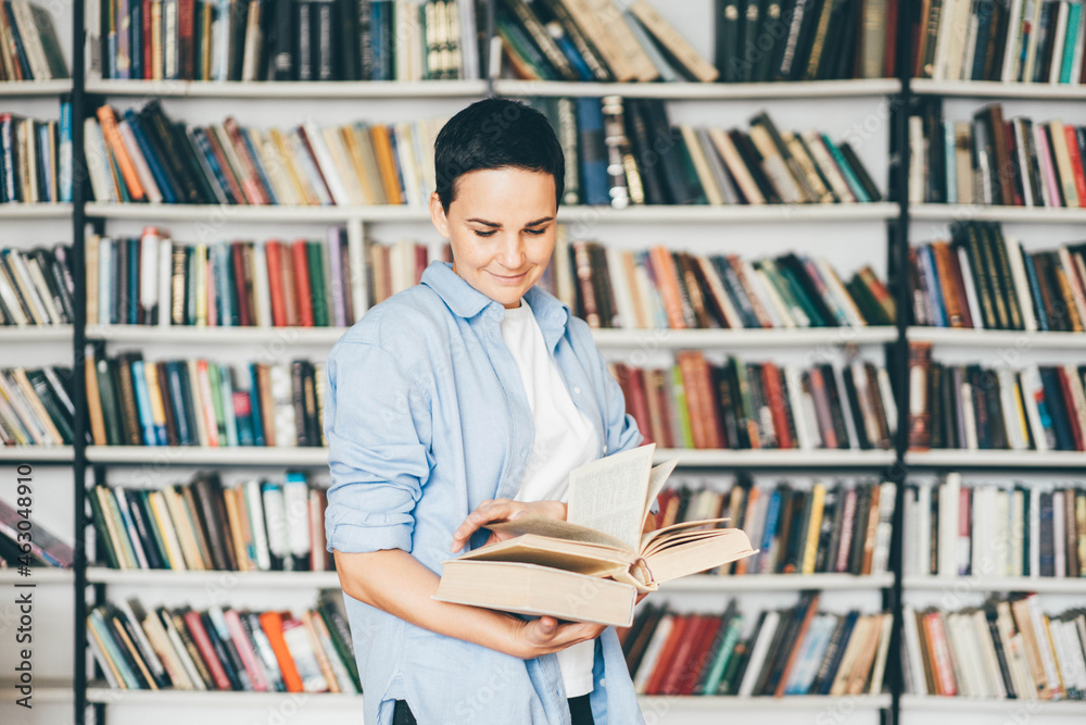 Young woman reading a book in front of bookshelves. Education concept. Young woman reading a book in front of bookshelves. Education concept.