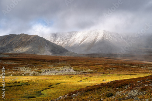 фотографія Autumn tundra and cold river on the background of misty snow-capped mountains, Arctic, Kola Peninsula
