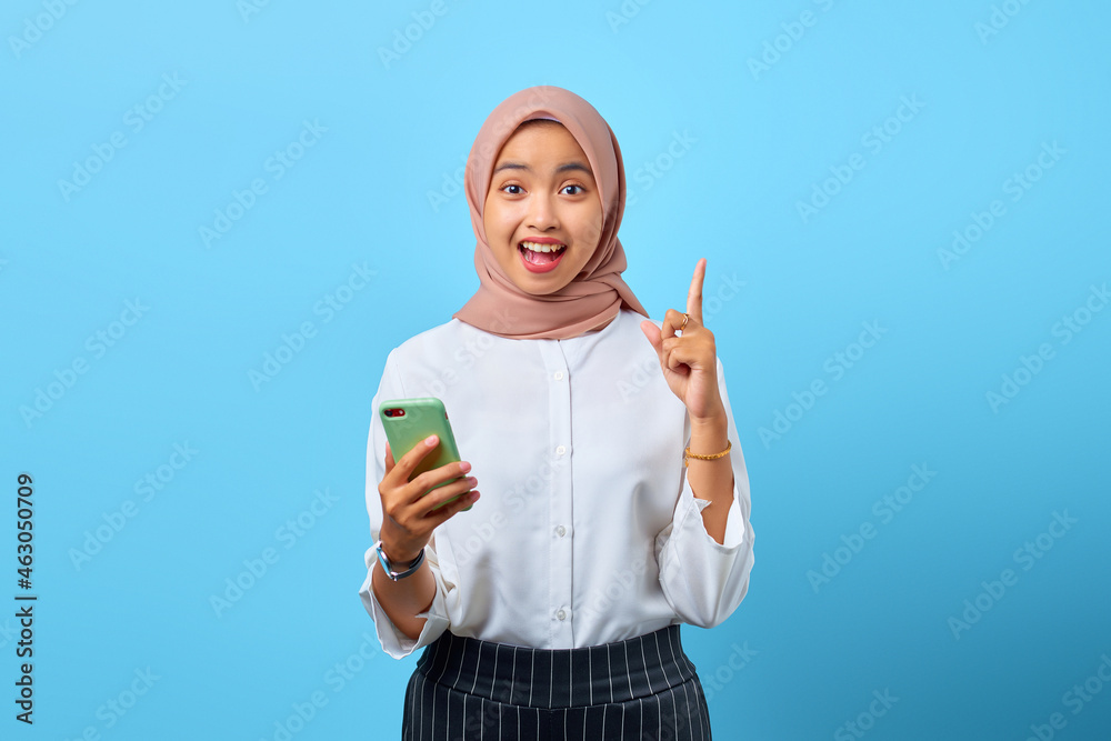 Portrait of excited young Asian woman holding mobile phone and raised finger because have solutions Portrait of excited young Asian woman holding mobile phone and raised finger because have solutions