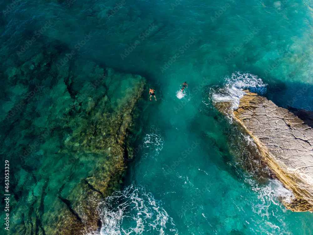 Aerial drone view of swimmers in the sea at summer. Tourists diving and swimming in the water. Transparent sea water in bay.