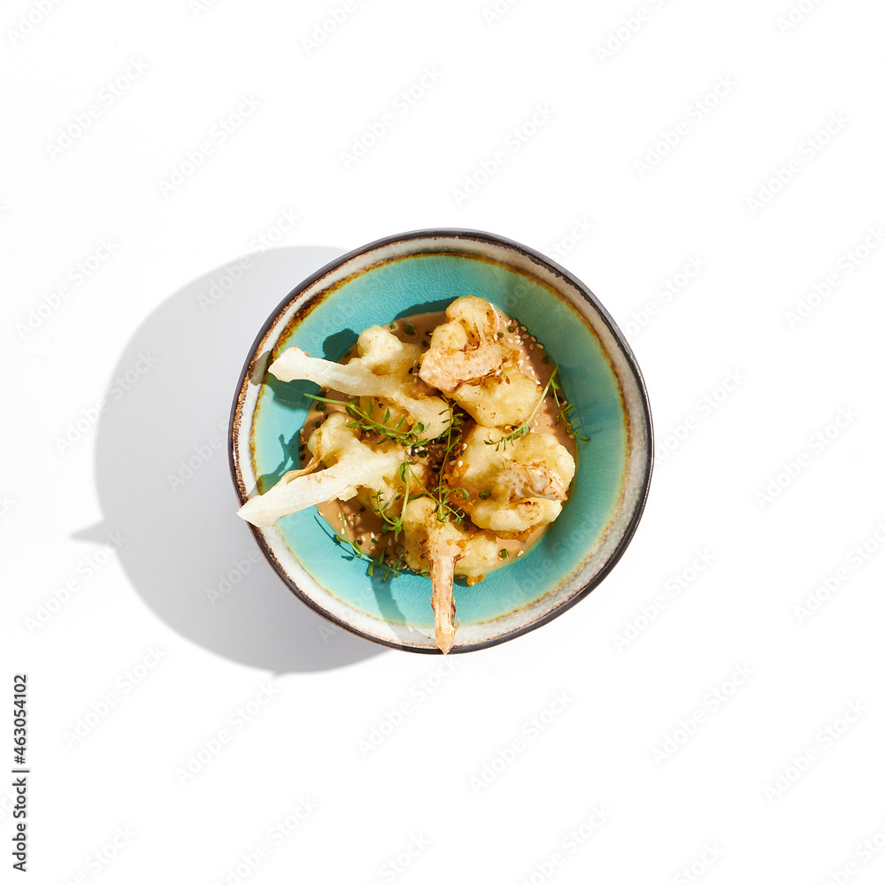 Fried tempura cauliflower with peanut sauce in bowl. Vegeterian hot dish - florets cabbages roasted in batter on white background. Veggie menu for asian restaurant. Hot vegan appetizers plant based. Fried tempura cauliflower with peanut sauce in bowl. Vegeterian hot dish - florets cabbages roasted in batter on white background. Veggie menu for asian restaurant. Hot vegan appetizers plant based.