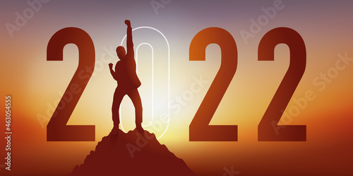 Carte de voeux 2022 montrant un homme levant le poing en signe de la victoire après avoir atteint son objectif en arrivant au sommet d’une montagne.