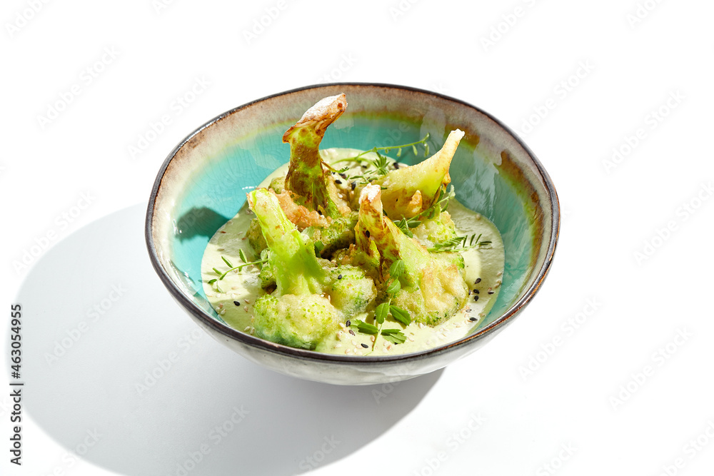 Fried tempura broccoli with peanut sauce in bowl. Vegeterian hot dish - florets cabbages roasted  in klar on white background. Veggie menu for asian restaurant. Hot vegan appetizers plant based.