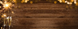 HAPPY NEW YEAR 2022 - Festive silvester background panorama banner long - Golden yellow fireworks, sparklers  and champagne classes toasting on rustic brown wooden wall texture with bokeh lights