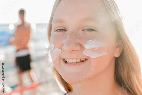 Close-up portrait of the face of a young positive attractive girl with sunscreen and sun protection on her cheeks