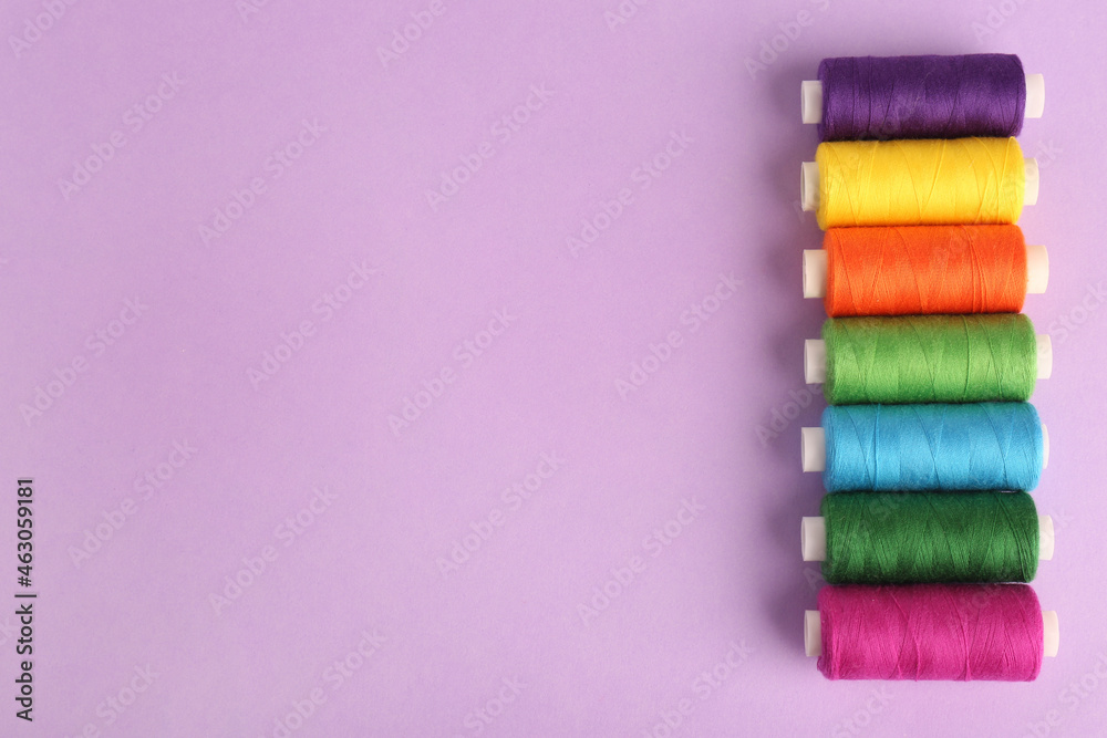 Different colorful sewing threads on lilac background, flat lay. Space for text Different colorful sewing threads on lilac background, flat lay. Space for text
