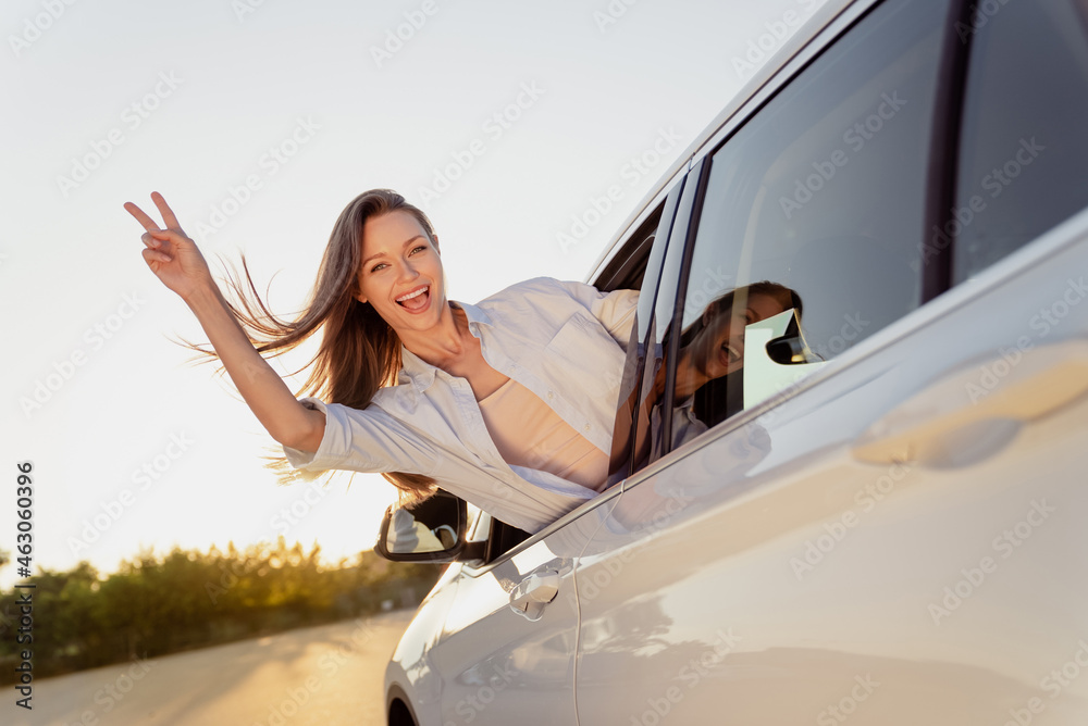 Photo portrait smiling woman riding in car with flying on wind hair showing v-sign gesture