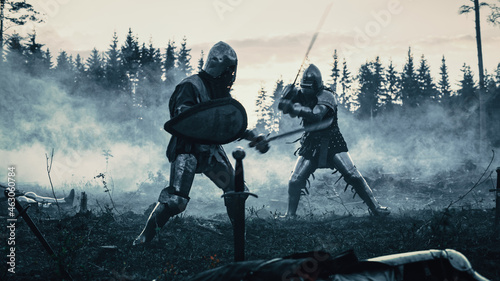 Dark Age Battlefield: Two Armored Medieval Knights Fighting with Swords. Battle of Armed Warrior Soldiers, Killing Enemy in Mysterious Forest. Cinematic Smoke, Mist, Light in Historic Reenactment