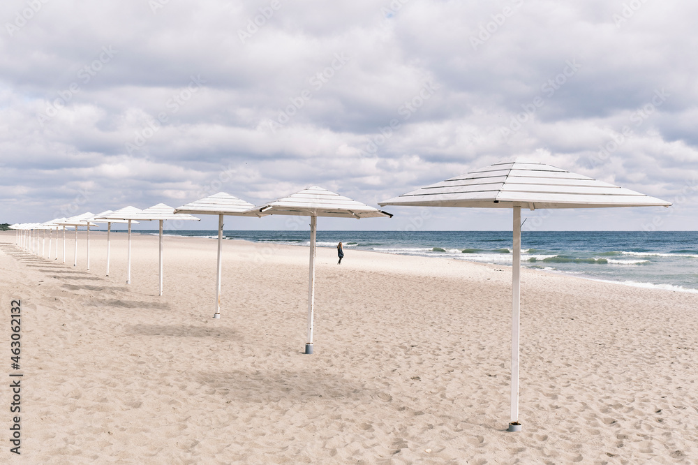 Baltic sandy beach with white wooden sun umbrellas in autumn. Seaside landscape