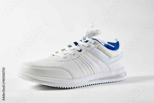 White sports sneakers with shoelace on a white wall background. Man sneakers for fitness. White sneaker with leather accents.