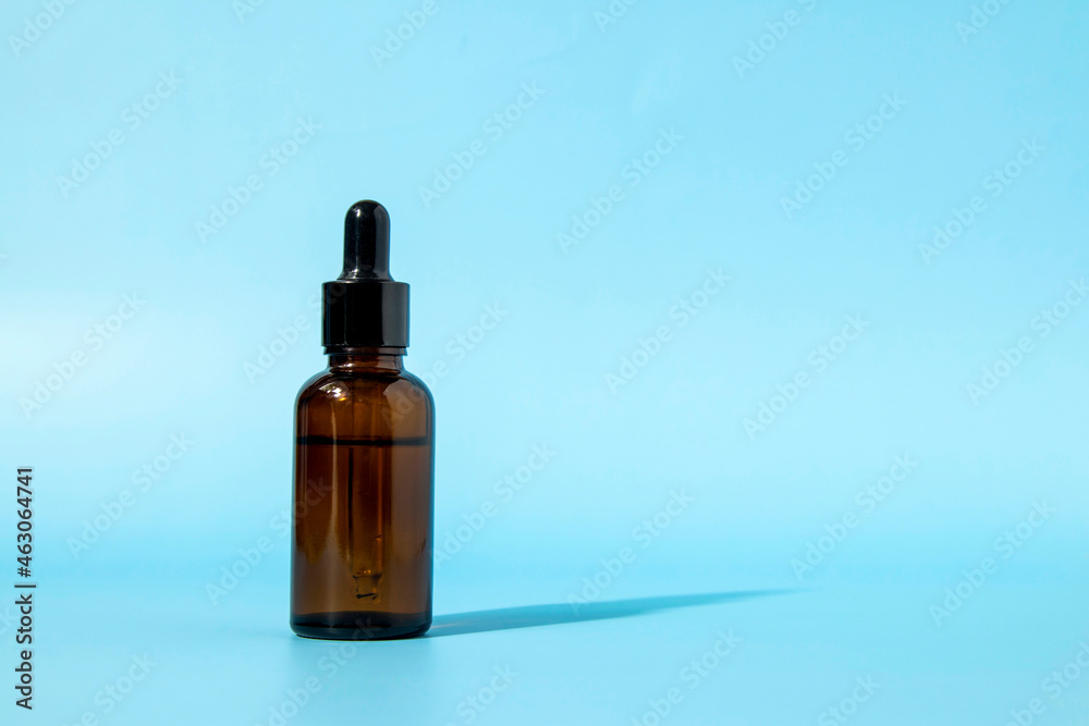 Glass dropper bottle made of brown glass on a blue background casts a shadow. Front view with copy space. Mockup of a cosmetic product. Serum for skin care.
