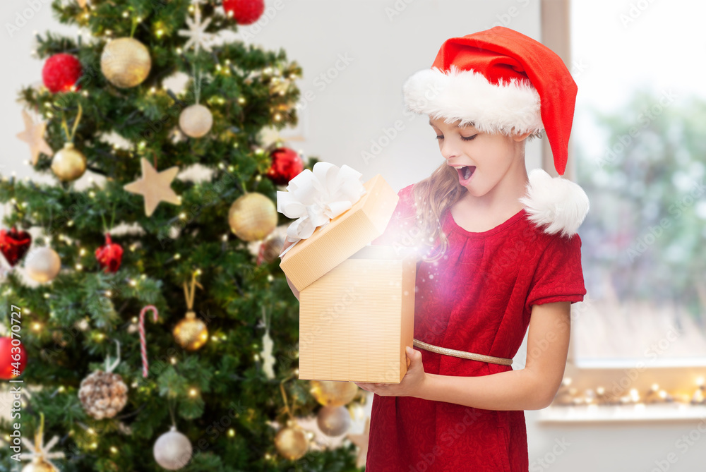 winter holidays and celebration concept - happy surprised girl opening gift box with fairy dust at home over christmas tree background