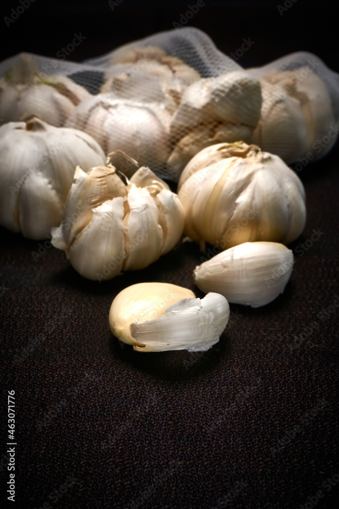 Head and mesh of garlic on a dark background, vertical frame Head and mesh of garlic on a dark background, vertical frame