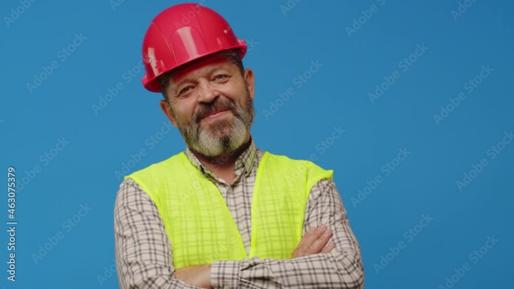Smiling senior man builder in vest and hardhat against blue background Smiling senior man builder in vest and hardhat against blue background