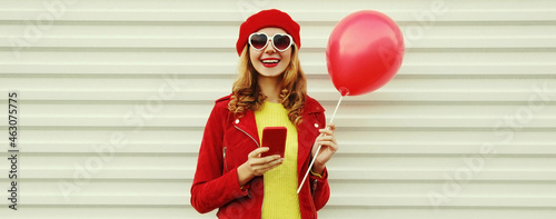 Portrait of happy smiling young woman with phone and red balloons wearing a beret on white background © rohappy
