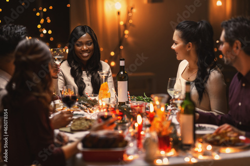 holidays, party and celebration concept - multiethnic group of happy friends having christmas dinner at home and drinking wine