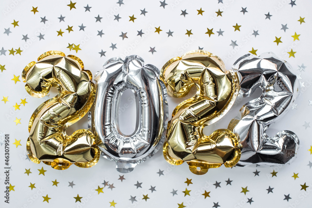 Banner. Happy New Year holiday. Balloons made of gold and silver foil with the number 2022 and confetti in the shape of stars on a white background. Flat lay. Banner. Happy New Year holiday. Balloons made of gold and silver foil with the number 2022 and confetti in the shape of stars on a white background. Flat lay.