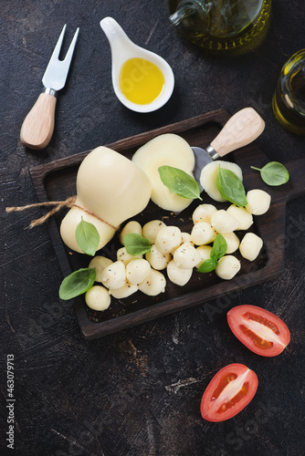 Above view of scamorza cheese with green basil leaves and olive oil, vertical shot on a dark-brown stone background