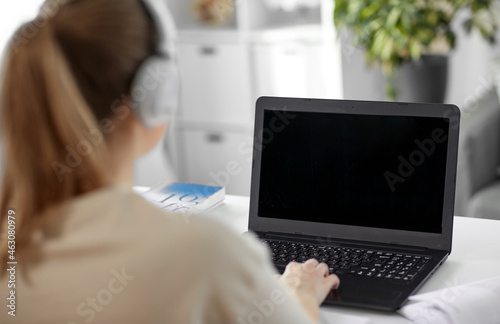 education, online school and distant learning concept - student woman in headphones with laptop computer, notebook and book at home
