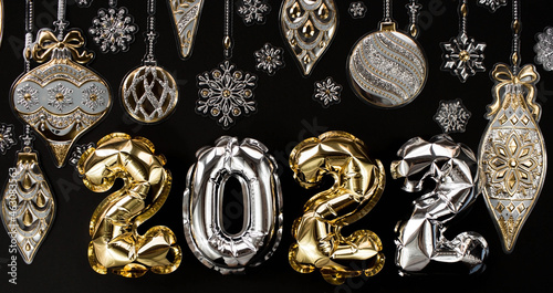 Banner. Happy New Year and Merry Christmas. Balloons made of gold and silver foil with the number 2022, snowflakes, garland and Christmas tree balls on a black background. Flat lay.