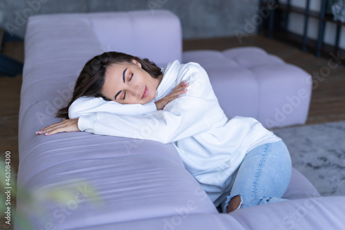 A young woman at home in a white hoodie on the couch sits peacefully, enjoys loneliness, comfort, alone, in a calm mood