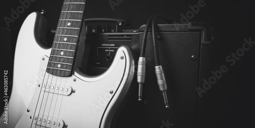 Black guitar amplifier with jack cable and silver electric guitar isolated on white background.
