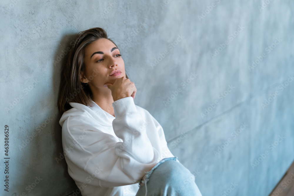 Young woman at home in a white hoodie sits on the stairs pensively dreamily looks Young woman at home in a white hoodie sits on the stairs pensively dreamily looks