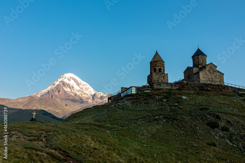 A view on Gergeti Trinity Church in Stepansminda, Georgia. The church is located on a high Caucasian mountain. Clear and blue sky above the church. In the back there are high mountain chains.