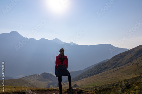 A woman enjoying the view on Caucasus mountains in Georgia. High mountain chains in front. There slopes are overgrown with green grass. Cloudless sky. Exploring new places photo