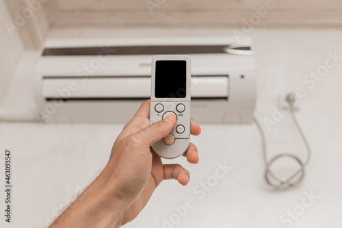 The guy's hand holds the remote control of the air conditioner. Cooling and temperature control in the room of the house