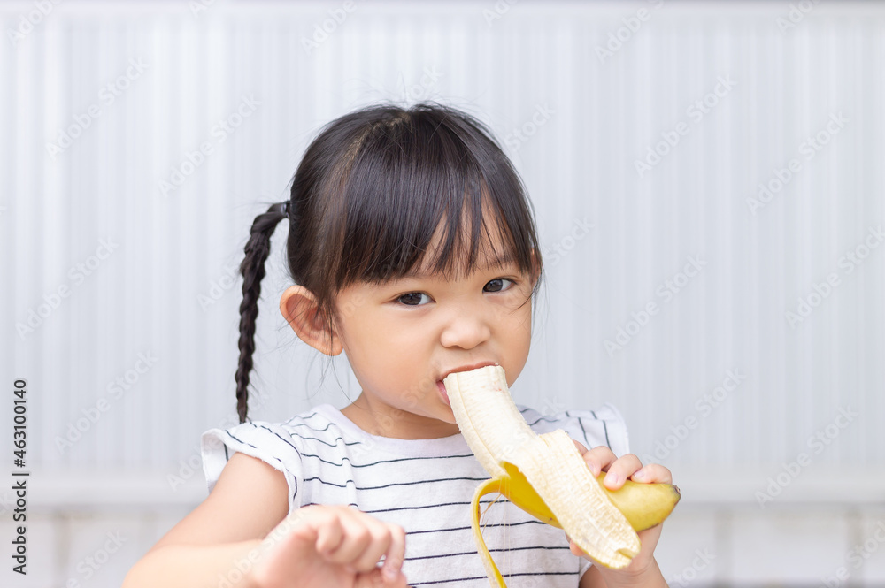 Portrait image of baby 3-4 years old. Happy Asian child girl enjoy eating a banana with sweet smiling. Food and healthy kids concept. Portrait image of baby 3-4 years old. Happy Asian child girl enjoy eating a banana with sweet smiling. Food and healthy kids concept.