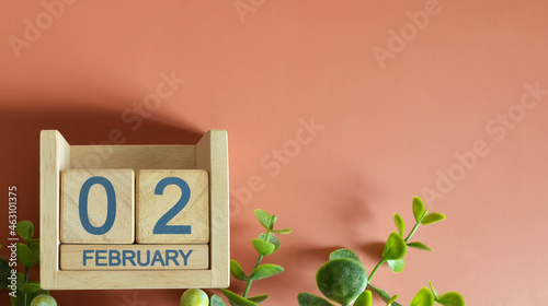February 2, Date design with calendar cube and leaf on orange background.