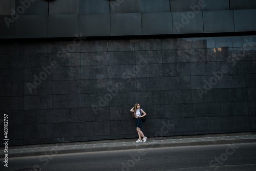 teenage girl with a backpack on the background of a large gray building