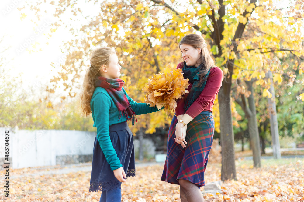 The daughter congratulates her mother and gives her an autumn bouquet of yellow leaves.