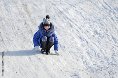 The girl squats and descends on her feet on a slippery snow slide.