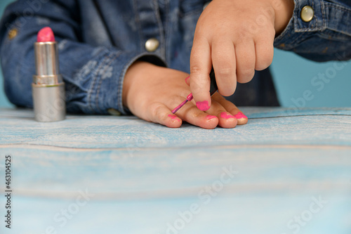 A small child ineptly paints his nails with nail polish.