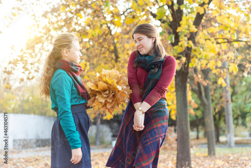 The daughter gives her mother a bouquet of yellow leaves on the background of autumn leaves in the park.