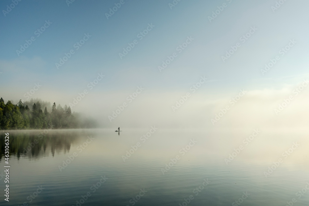 Standup paddle boarder on a foggy forest lake