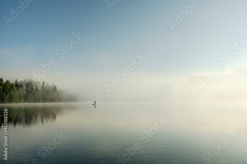 Standup paddle boarder on a foggy forest lake