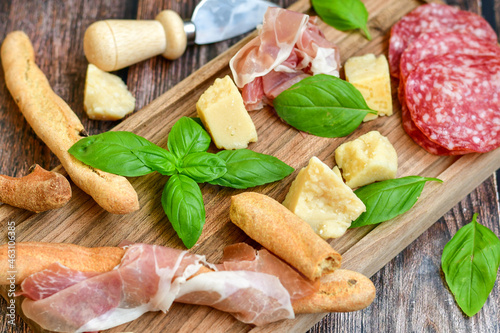 Italian dried thinly sliced artisan pork salami Milano , parmesan cheese, tomatoes and fresh basil on wooden background .Rustic home made italian snack.